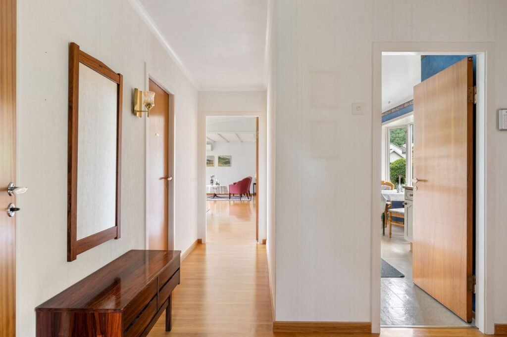 A well-lit modern hallway with open doors leading to a bright living area and garden view.