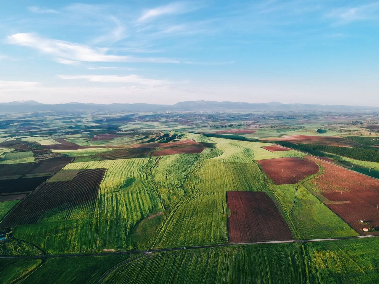 Expansive aerial landscape of green and brown agricultural fields under a clear blue sky.